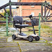 Motion Healthcare Lithilite Scooter with puncture proof wheels and black seat parked outdoors by a pond, side view.