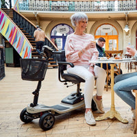 Older woman sitting on a Motion Healthcare Lithilite Scooter, drinking coffee at an indoor café table, in use.