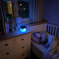 Lifemax Mood Light Bluetooth Speaker on dresser next to teddy bear and books, child sleeping nearby, in use.