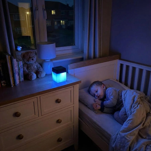 Lifemax Mood Light Bluetooth Speaker on dresser next to teddy bear and books, child sleeping nearby, in use.