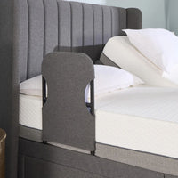 Upholstered bed with Opera Beds Motion Bed Grab Rail, raised mattress, white pillows and bedding, side view.