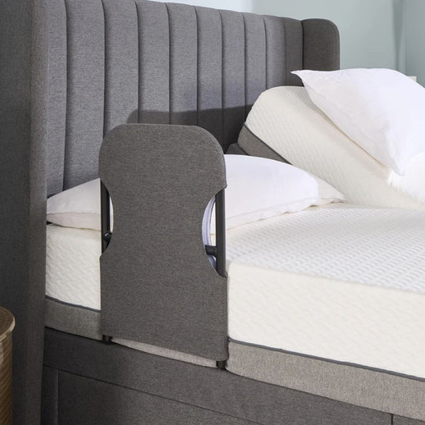 Upholstered bed with Opera Beds Motion Bed Grab Rail, raised mattress, white pillows and bedding, side view.