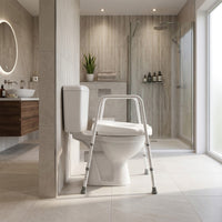 NRS Mowbray Width Adjustable Toilet Seat & Frame in modern bathroom next to glass shower and wall-mounted sink, sunlit windows, wide view.