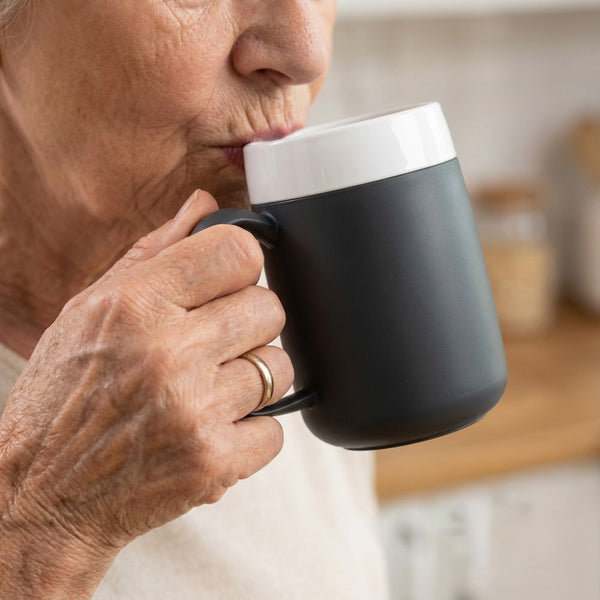 Older adult using ORNAMIN Mug with Internal Cone, holding with both hands indoors, in use.