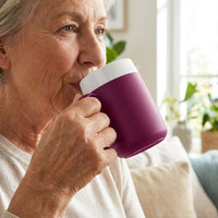 Older woman indoors sipping from an ORNAMIN Mug with Internal Cone, bright room with plants in background, in use.
