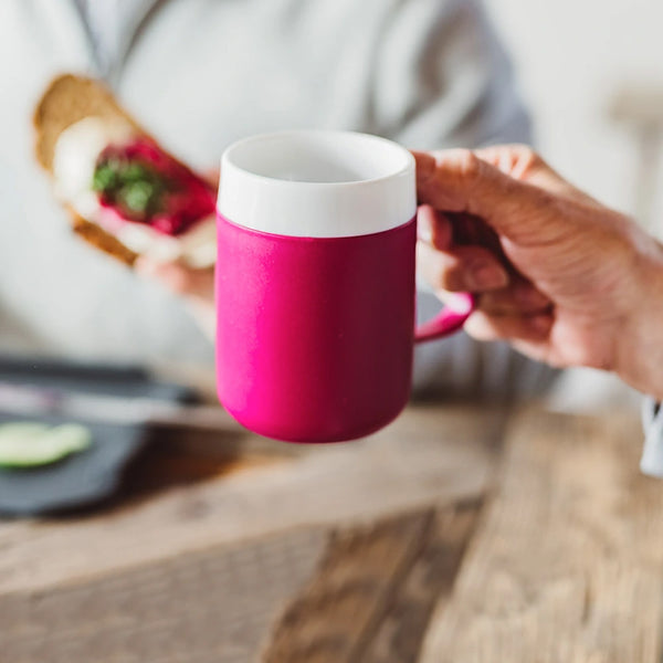 Person holding ORNAMIN Mug with Internal Cone as another eats a sandwich at a wooden table, in use view.
