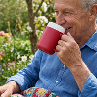 Older man in blue shirt drinking from an ORNAMIN Mug with Internal Cone, sitting outside with colourful blanket, in use view.