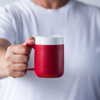 Person in a white shirt holding an ORNAMIN Mug with Internal Cone and white lid, extended toward the camera, close-up.