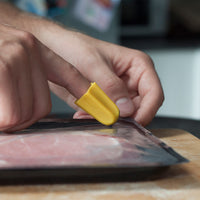 RNIB Nimble One-Finger Cutting Tool opening sliced meat packaging on a wooden surface, in use.