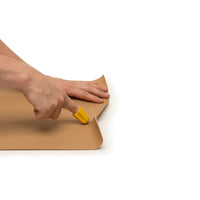 Hands cutting paper with the RNIB Nimble One-Finger Cutting Tool, white background, in use view.