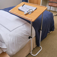 NRS Divan Overbed Table with papers, pen, thermometer and magnifying glass on bedding, in use view.