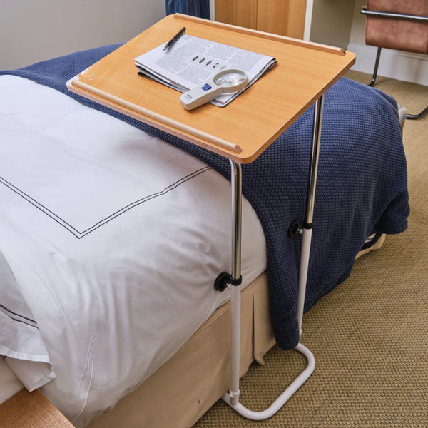 NRS Divan Overbed Table with papers, pen, thermometer and magnifying glass on bedding, in use view.