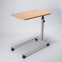 Height adjustable overbed table with light wood top, metal base and four castors, for home use, angled side view.