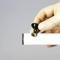 Hand holding a black screw above the NRS Overbed/Overchair Table, assembling the white metal tube, close-up.