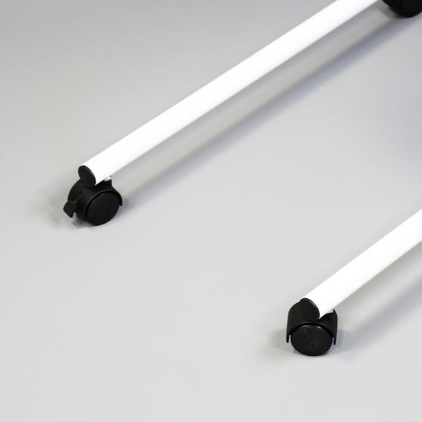 Pair of white metal rods with black caster wheels from NRS Overbed/Overchair Table on light grey surface, close-up.