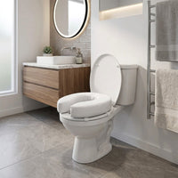 Homecraft Padded Raised Toilet Seat on toilet in modern bathroom, wooden sink cabinet, round mirror, towels on rack, front view.