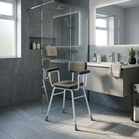 Drive Perching Stool with padded arms and backrest by the shower in a modern bathroom, sink and mirror visible, wide view.