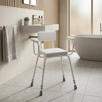 Drive Perching Stool with padded arms and backrest positioned by sink and bathtub in modern bathroom, side view.