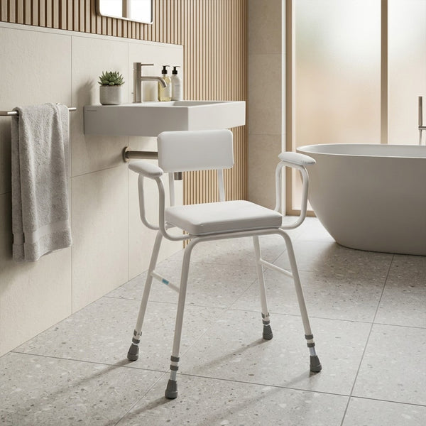 Drive Perching Stool with padded arms and backrest positioned by sink and bathtub in modern bathroom, side view.
