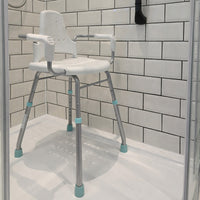 Gordon Ellis Prima shower stool with arms and back for support in a tiled shower, positioned near a corner drain, front angle view.