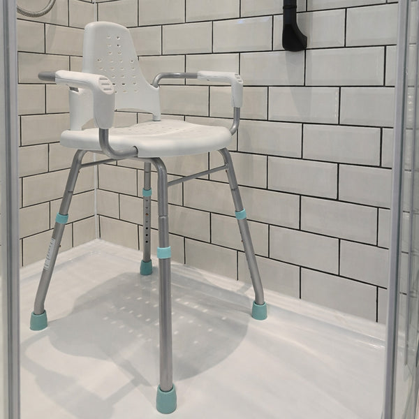 Gordon Ellis Prima shower stool with arms and back for support in a tiled shower, positioned near a corner drain, front angle view.