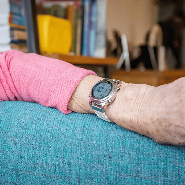 Older adult wearing a Ravencourt Living Radio Controlled Digital Talking Watch, seated on couch with blurred books in background, in use.