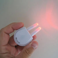 Hand holding Lifemax Rechargeable Hay Fever and Allergy Reliever with LED prongs lit, light on wall, in use view.