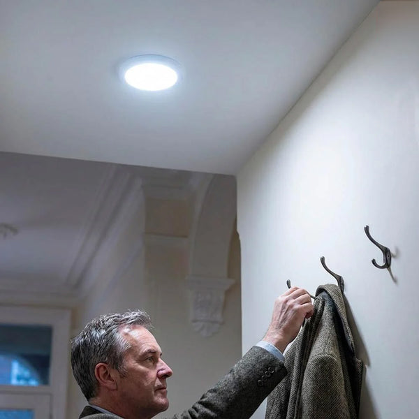 Lifemax Rechargeable Motion Ceiling Light installed above man hanging coat on wall hook in hallway, in use.