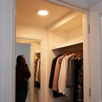Lifemax Rechargeable Motion Ceiling Light lighting up a closet with a woman standing nearby, in use view.
