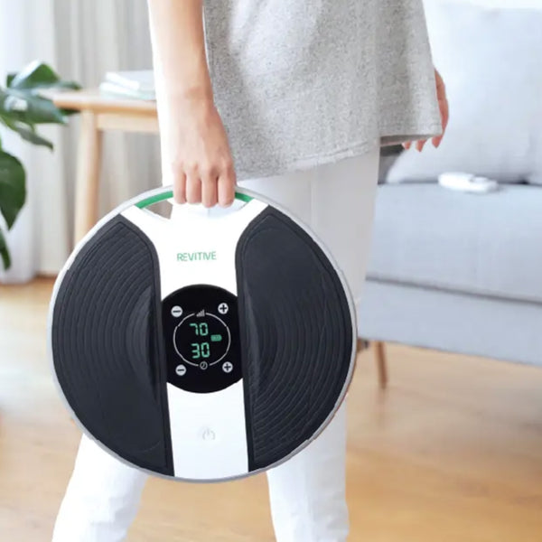 Person holding Revitive New Medic circulation booster in a bright living room, in use.