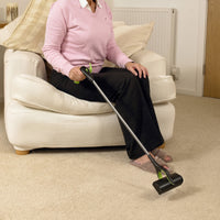 Person seated on a white armchair using RevoReach GripLock to pick up an item from beige carpet, in use.