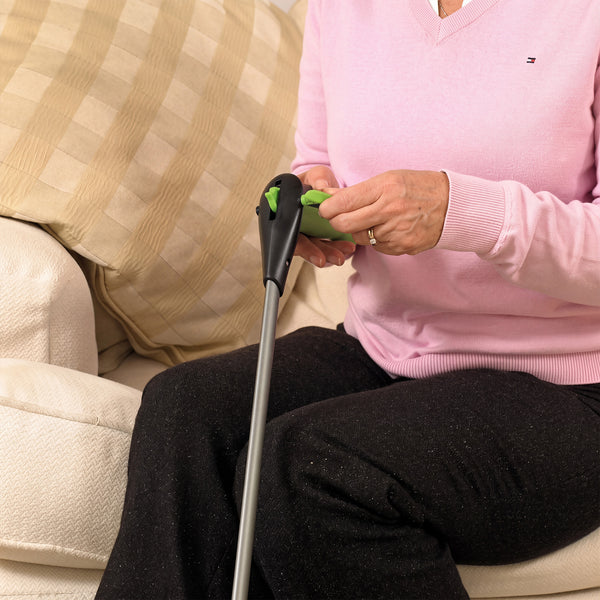 Person in pink sweater using RevoReach GripLock on cream sofa with striped cushion, in use view.