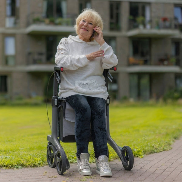 Elderly woman using Rollz Air Carbon Fibre Rollator, talking on phone outside flats, in use.