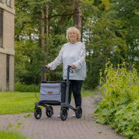 Older woman with light hair using Rollz Air Carbon Fibre Rollator on a garden path among greenery, in use.