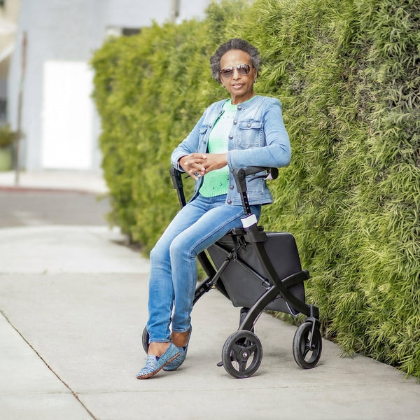 Woman sitting on a Rollz Flex 2-in-1 Rollator and Shopping Trolley on pavement, front view.