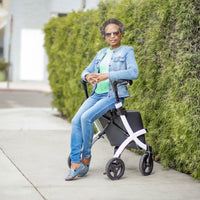 Rollz Flex 2-in-1 Rollator and Shopping Trolley in Jungle Green with woman sitting, wearing jeans, denim jacket and sunglasses, side view.