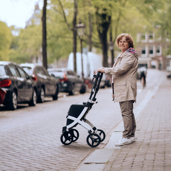 Older woman using a Jungle Green Rollz Flex 2-in-1 rollator and shopping trolley on city pavement, in use view.