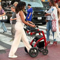 Woman using Rollz Motion Performance rollator at a busy city crosswalk, pedestrians and cars visible, in use view.