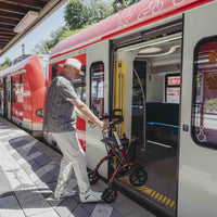Older man using a Saljol Allround Bariatric Rollator boarding a train at an outdoor station, in use view.