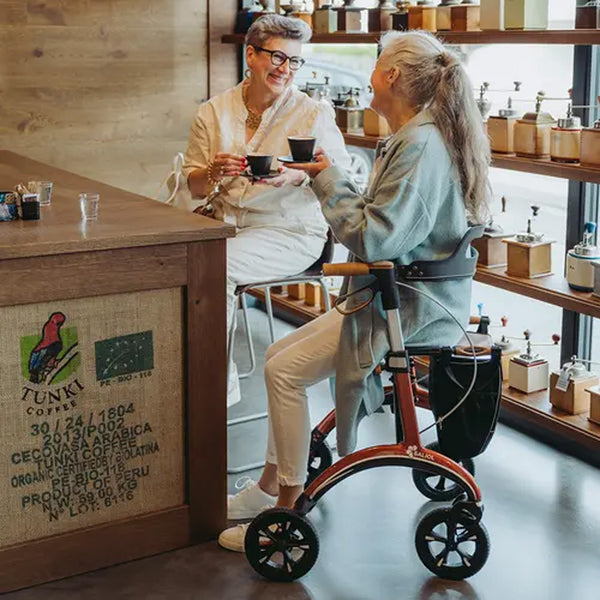 Saljol Carbon Rollator used by older woman at cafe with shelves behind, in use.