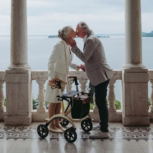 Elderly couple on a balcony, woman using a Saljol Carbon Rollator for support, in use view.