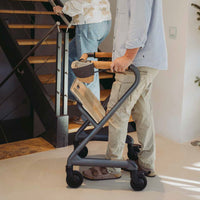 Saljol Indoor Rollator in use by a person near stairs at home, another person walking up the staircase, side view.