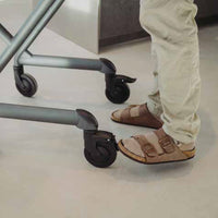 Person in sandals and beige trousers standing beside a Saljol Indoor Rollator on a smooth floor, side view.