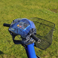 Able2 Scooter Control Panel Cover fitted over handlebar with attached wire basket, parked on grass, front view.