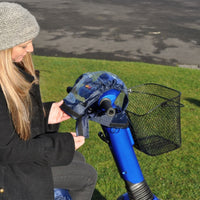 Able2 Scooter Control Panel Cover being adjusted on mobility scooter handlebars with wire basket, user wearing beanie, in use view.