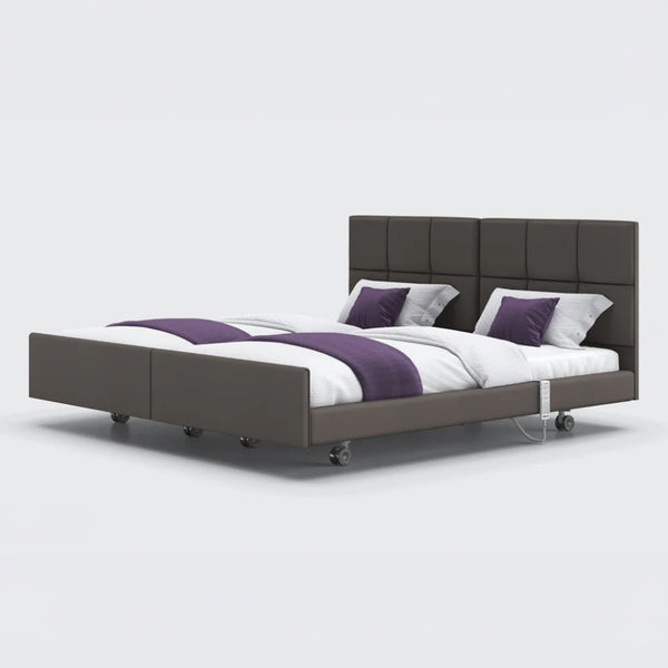 Profiling bed with padded headboard, wheels, and purple and white bedding, front view.