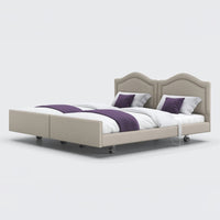 Opera Beds Signature Comfort Dual Profiling Bed with curved headboards, wheels, white bedding and purple throws, front view.