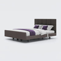 Dual profiling bed in leatherette with padded headboard, frame and castor wheels, front view.