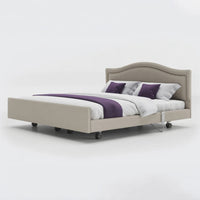 Opera Beds Signature Comfort Dual Profiling Bed with wheels and white bedding, purple accents, linen fabric finish, angled side view.