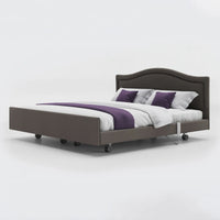 Dual profiling bed with leatherette headboard, white bedding, and wheels on the base, front view.